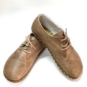May include: A pair of brown leather lace-up shoes with a stitched edge. The shoes have a casual, comfortable look.