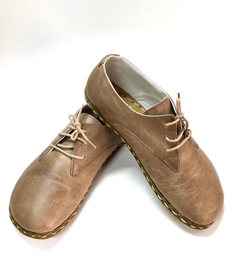 May include: A pair of brown leather lace-up shoes with a stitched edge. The shoes have a casual, comfortable look.