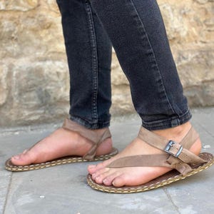 Puede incluir: Un par de sandalias de cuero marr&oacute;n con una hebilla y un borde cosido. Las sandalias tienen un dise&ntilde;o sencillo y est&aacute;n hechas de cuero de alta calidad.