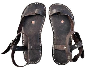 May include: A pair of brown leather sandals with ankle straps and buckles. The sandals have a simple design with a single strap across the toe and a strap around the ankle.