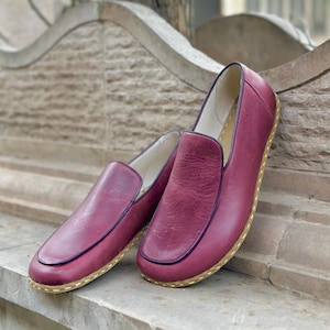 Puede incluir: Un par de zapatos de cuero burdeos de vestir sin cordones con suela marr&oacute;n claro. Los zapatos tienen un dise&ntilde;o sencillo con un sutil detalle de costura alrededor del borde.