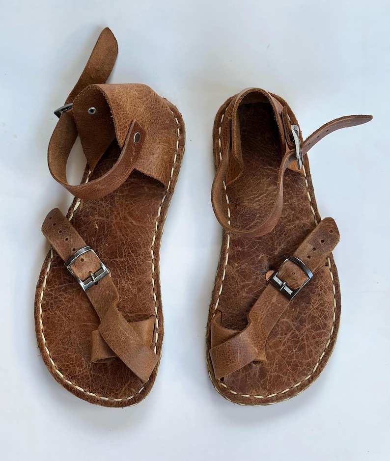 May include: A pair of brown leather sandals with buckles and straps. The sandals have a simple design and are made of high-quality leather.