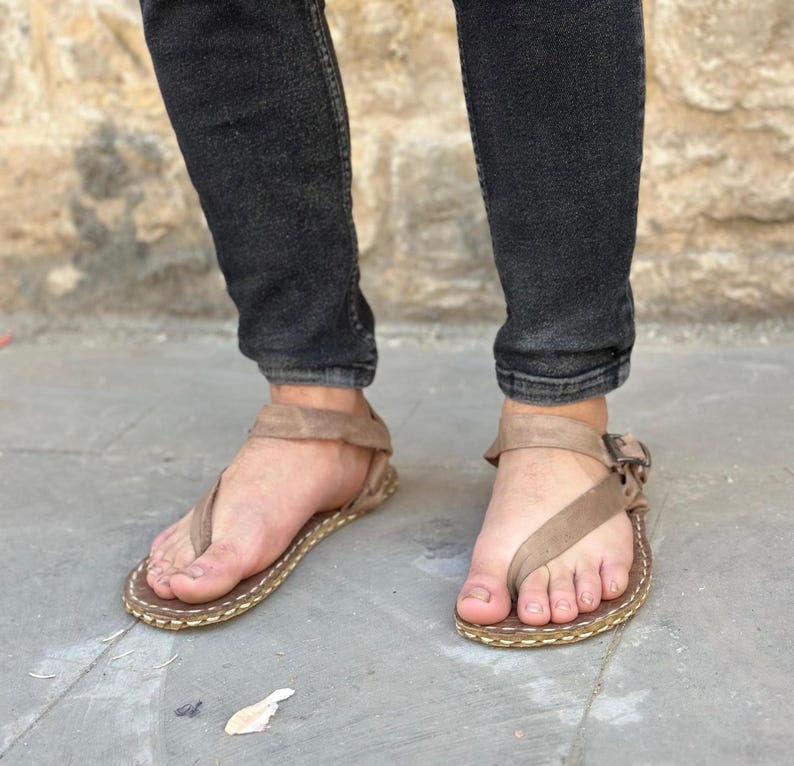 Puede incluir: Un par de sandalias de cuero marr&oacute;n con una correa sobre el pie y una hebilla en el tobillo.