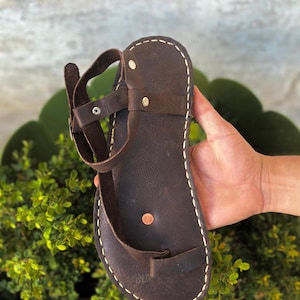 May include: Brown leather sandals with a single strap and a white stitch detail around the edge.