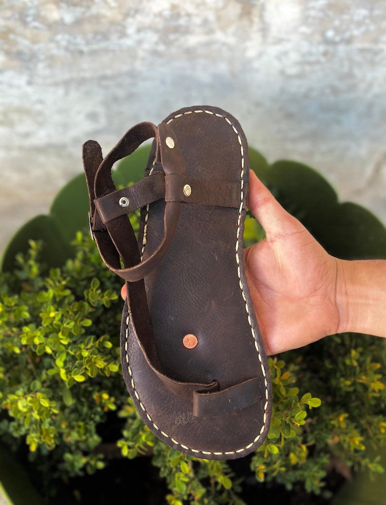 May include: Brown leather sandals with a single strap and a white stitch detail around the edge.