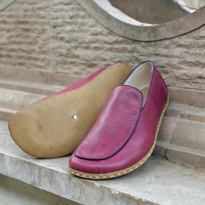 Puede incluir: Un par de zapatos de cuero burdeos de vestir sin cordones con ribete azul oscuro y suela marr&oacute;n claro.