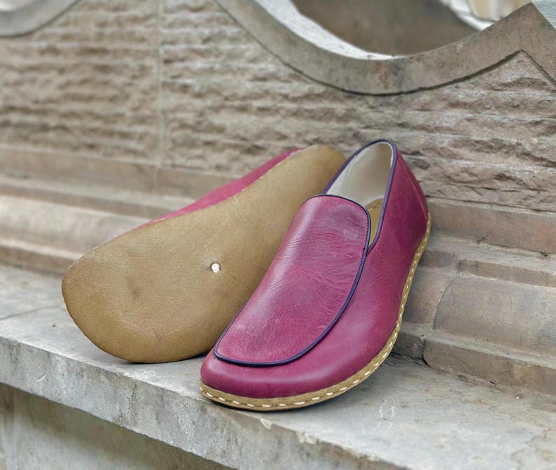 Puede incluir: Un par de zapatos de cuero burdeos de vestir sin cordones con ribete azul oscuro y suela marr&oacute;n claro.