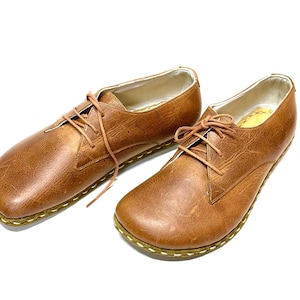 May include: A pair of brown leather lace-up shoes with a stitched edge on the sole.