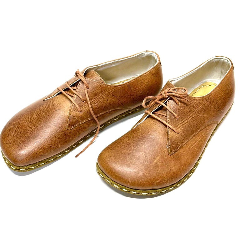 May include: A pair of brown leather lace-up shoes with a stitched edge on the sole.