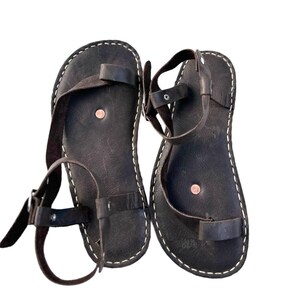 May include: A pair of brown leather sandals with adjustable straps. The sandals have a simple design and are made of high-quality leather.