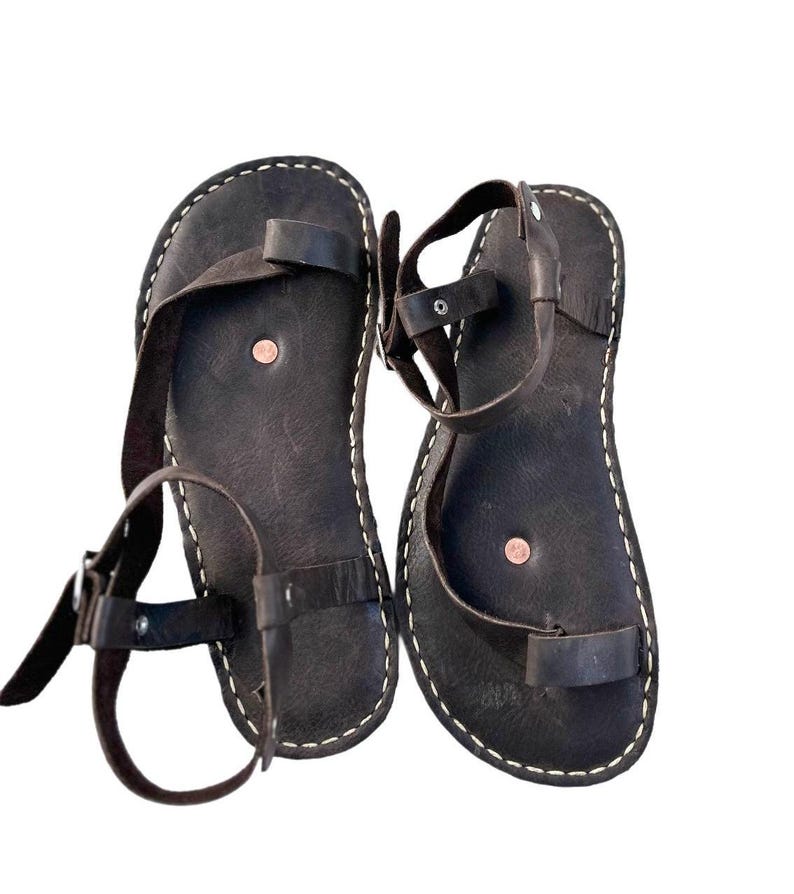 May include: A pair of brown leather sandals with adjustable straps. The sandals have a simple design and are made of high-quality leather.