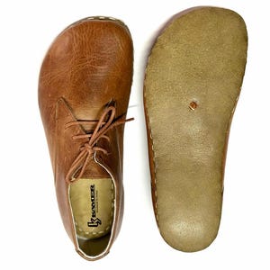 May include: A pair of brown leather lace-up shoes with a white sole. The shoes have a brown leather insole with the text "Kreater" printed on it.