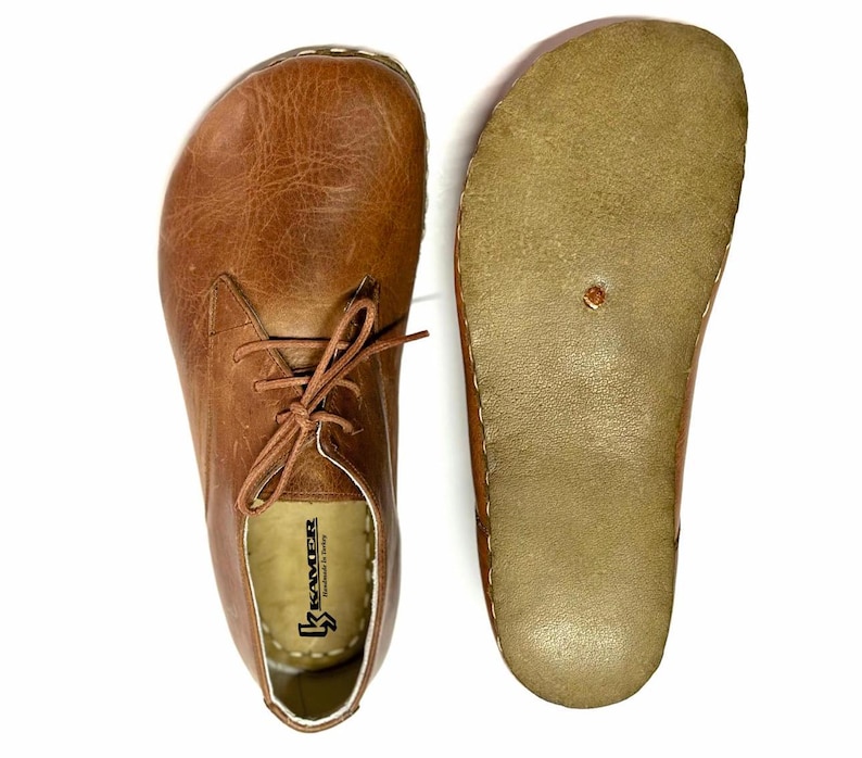 May include: A pair of brown leather lace-up shoes with a white sole. The shoes have a brown leather insole with the text "Kreater" printed on it.
