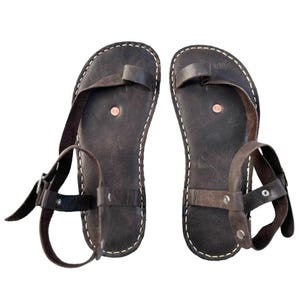 May include: A pair of brown leather sandals with ankle straps and buckles. The sandals have a simple design with a single strap across the toe.