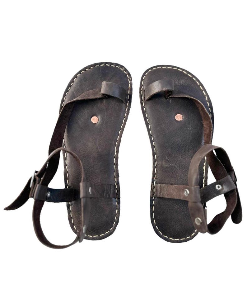 May include: A pair of brown leather sandals with ankle straps and buckles. The sandals have a simple design with a single strap across the toe.