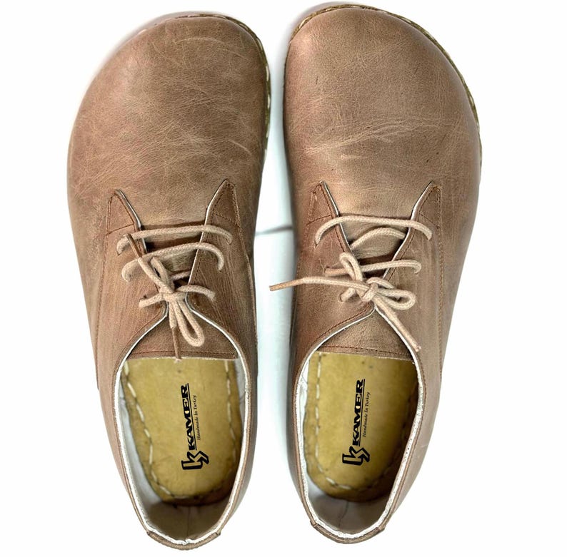 May include: A pair of brown leather lace-up shoes with white stitching around the edges. The shoes have a brown leather sole and are made by the brand "Kramer".