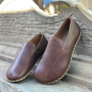 K&ouml;nnte beinhalten: Ein Paar braune Slipper aus Leder mit einer gen&auml;hten Naht um die Sohle.