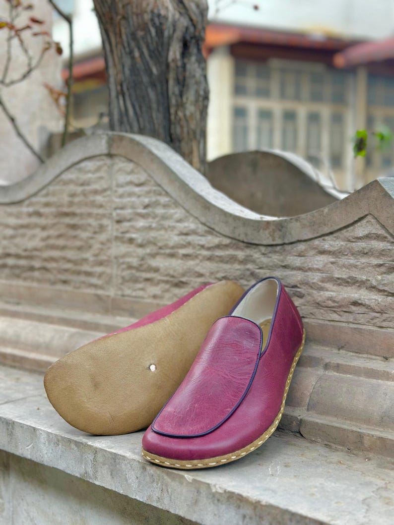 Puede incluir: Un par de zapatos de cuero burdeos de vestir sin cordones con un borde cosido y una suela marr&oacute;n claro.