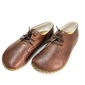May include: A pair of brown leather lace-up shoes with a rounded toe and a stitched edge.