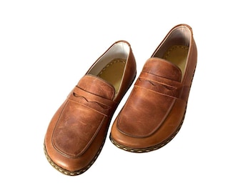 May include: A pair of brown leather penny loafers. The shoes feature a classic design with a rounded toe, a strap across the vamp, and a stitched sole. The leather has a distressed appearance.