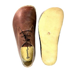 May include: A pair of brown leather lace-up shoes with a light brown sole. The shoes have a brand label that reads "K-Sater" inside.