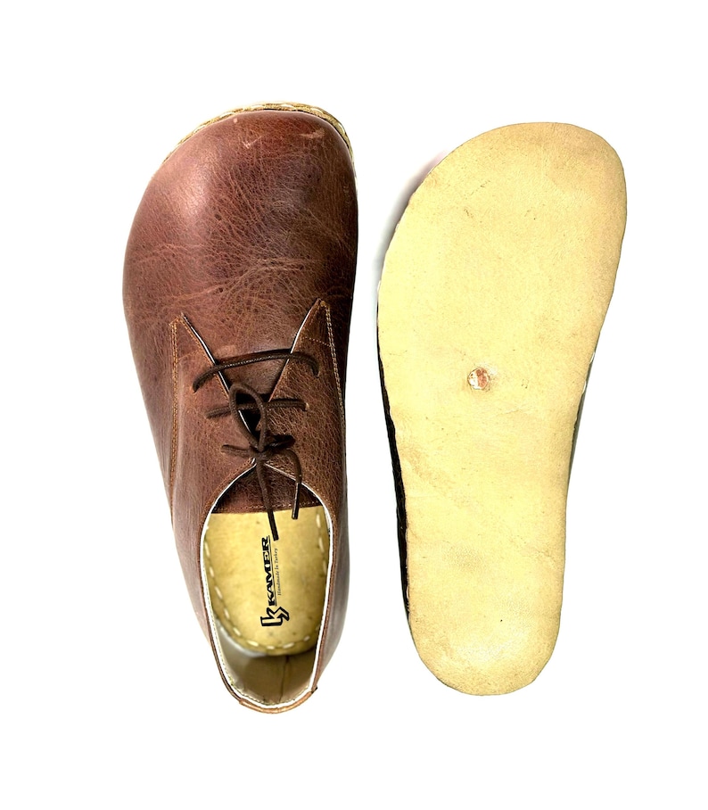 May include: A pair of brown leather lace-up shoes with a light brown sole. The shoes have a brand label that reads "K-Sater" inside.