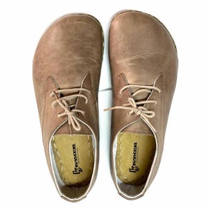 May include: A pair of brown leather lace-up shoes with a white sole. The shoes have a simple design and are made by the brand "Kramer".