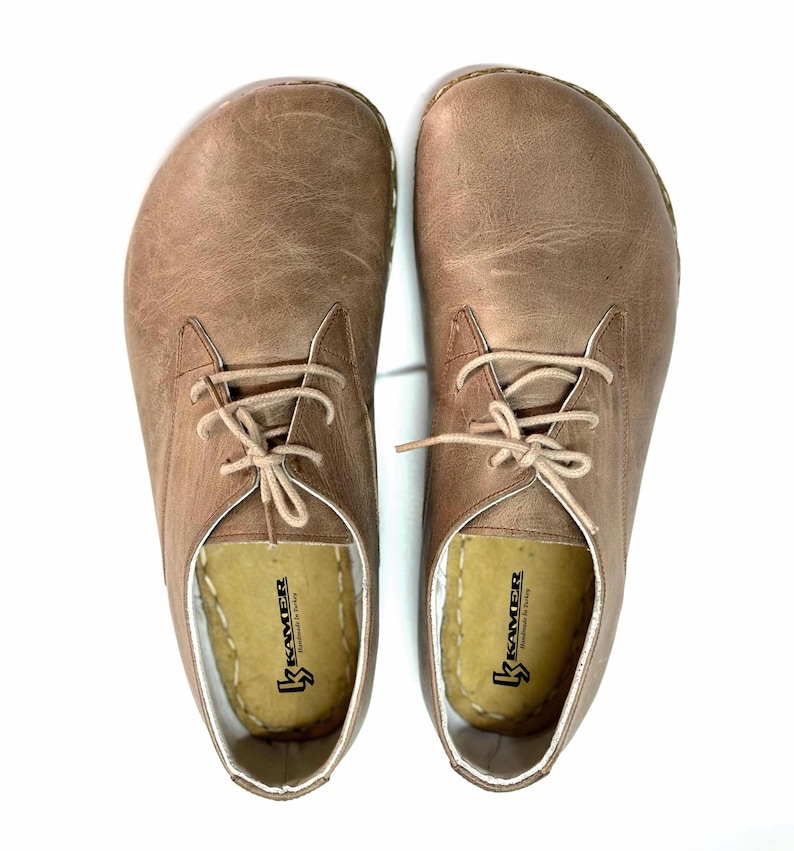 May include: A pair of brown leather lace-up shoes with a white sole. The shoes have a simple design and are made by the brand "Kramer".