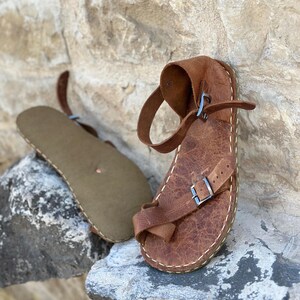 May include: A pair of brown leather sandals with buckles. The sandals have a simple design and are made of high-quality leather.