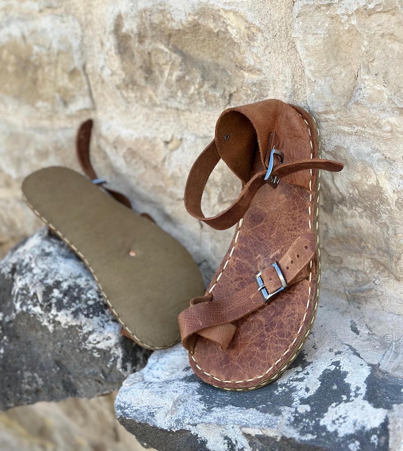 May include: A pair of brown leather sandals with buckles. The sandals have a simple design and are made of high-quality leather.