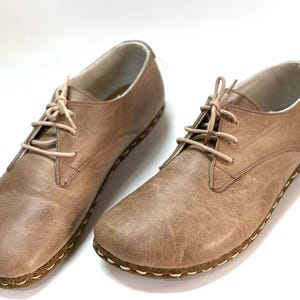 May include: A pair of light brown leather lace-up shoes with a stitched edge around the sole.