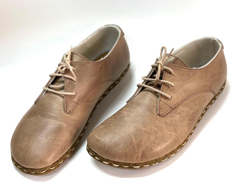 May include: A pair of light brown leather lace-up shoes with a stitched edge around the sole.