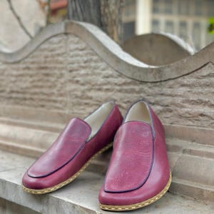 Puede incluir: Un par de zapatos de cuero burdeos de vestir sin cordones con suela cosida de color marr&oacute;n claro.
