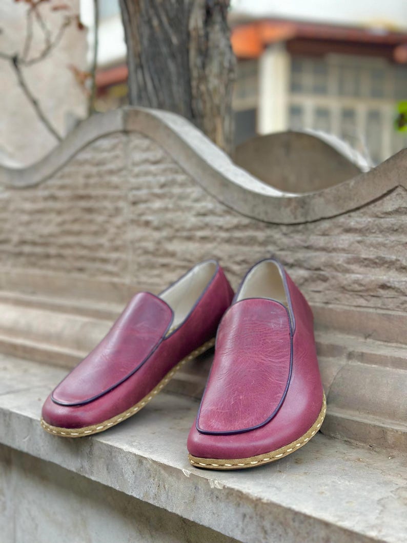 Puede incluir: Un par de zapatos de cuero burdeos de vestir sin cordones con suela cosida de color marr&oacute;n claro.