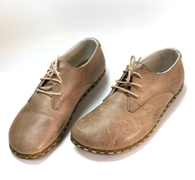May include: A pair of light brown leather lace-up shoes with a stitched edge. The shoes have a casual, comfortable look.