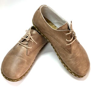 May include: A pair of brown leather lace-up shoes with a stitched edge. The shoes have a casual, minimalist style.