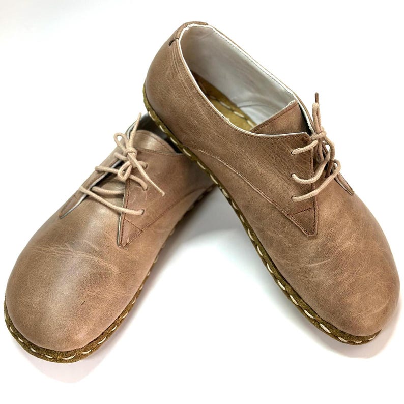 May include: A pair of brown leather lace-up shoes with a stitched edge. The shoes have a casual, minimalist style.