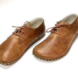 May include: A pair of brown leather lace-up shoes with a stitched edge on the sole.
