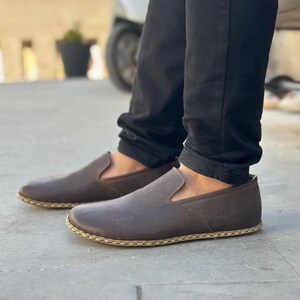 May include: A pair of brown leather slip-on shoes with a stitched edge detail. The shoes have a casual, comfortable look.