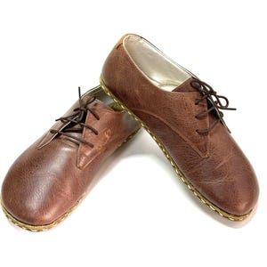 May include: A pair of brown leather lace-up shoes with a gold stitching detail around the sole.