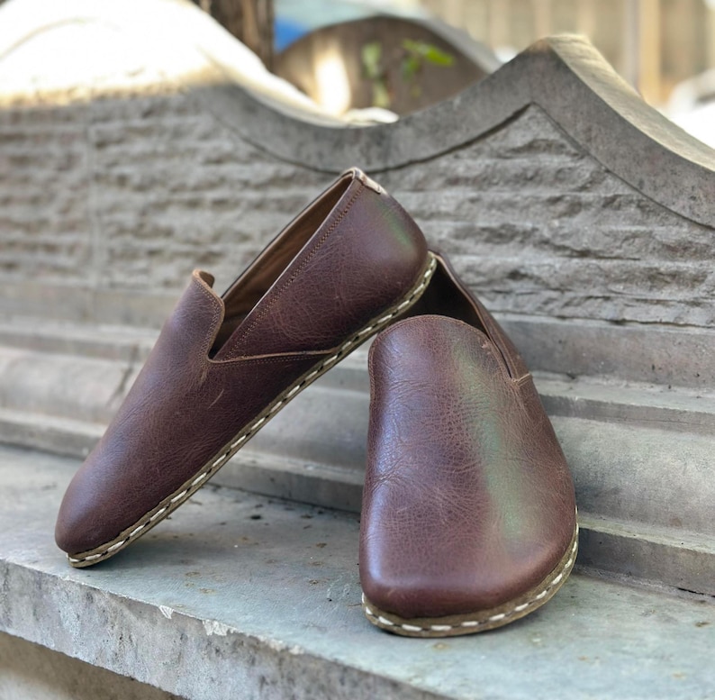 K&ouml;nnte beinhalten: Ein Paar braune Slipper aus Leder mit wei&szlig;en N&auml;hten an der Sohle.
