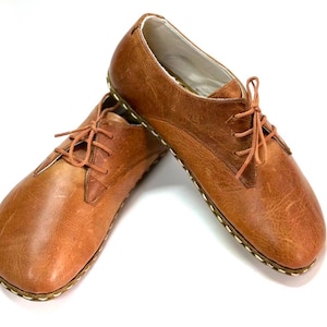May include: A pair of brown leather lace-up shoes with a rounded toe and a stitched sole.