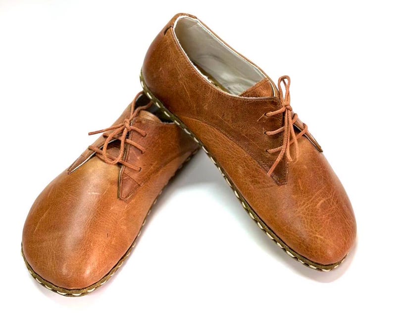 May include: A pair of brown leather lace-up shoes with a rounded toe and a stitched sole.
