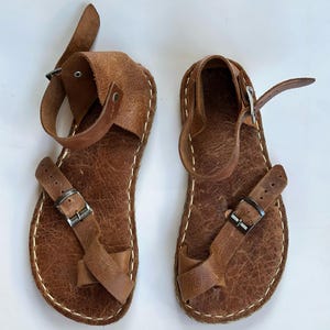 May include: A pair of brown leather sandals with buckle closures. The sandals have a simple design and are made of high-quality leather.