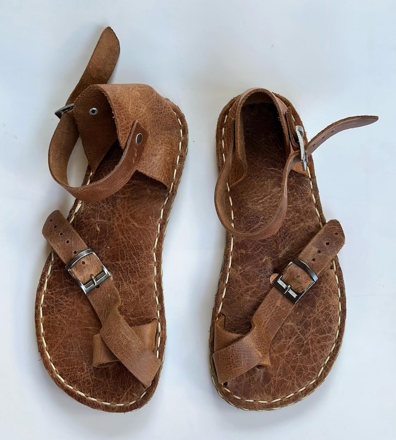 May include: A pair of brown leather sandals with buckle closures. The sandals have a simple design and are made of high-quality leather.