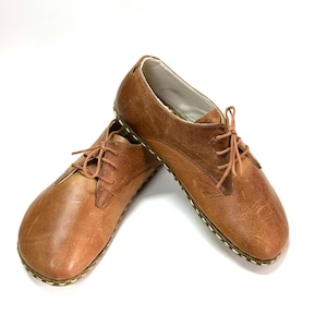 May include: A pair of brown leather lace-up shoes with a stitched edge on the sole.
