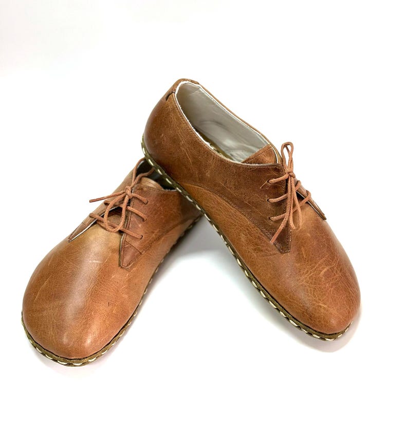 May include: A pair of brown leather lace-up shoes with a stitched edge on the sole.