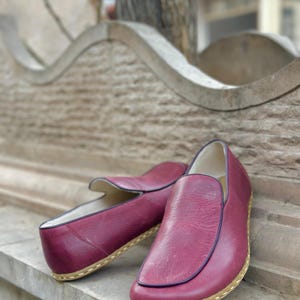 Puede incluir: Un par de zapatos de cuero burdeos con suela marr&oacute;n claro. Los zapatos est&aacute;n sobre una superficie de piedra.