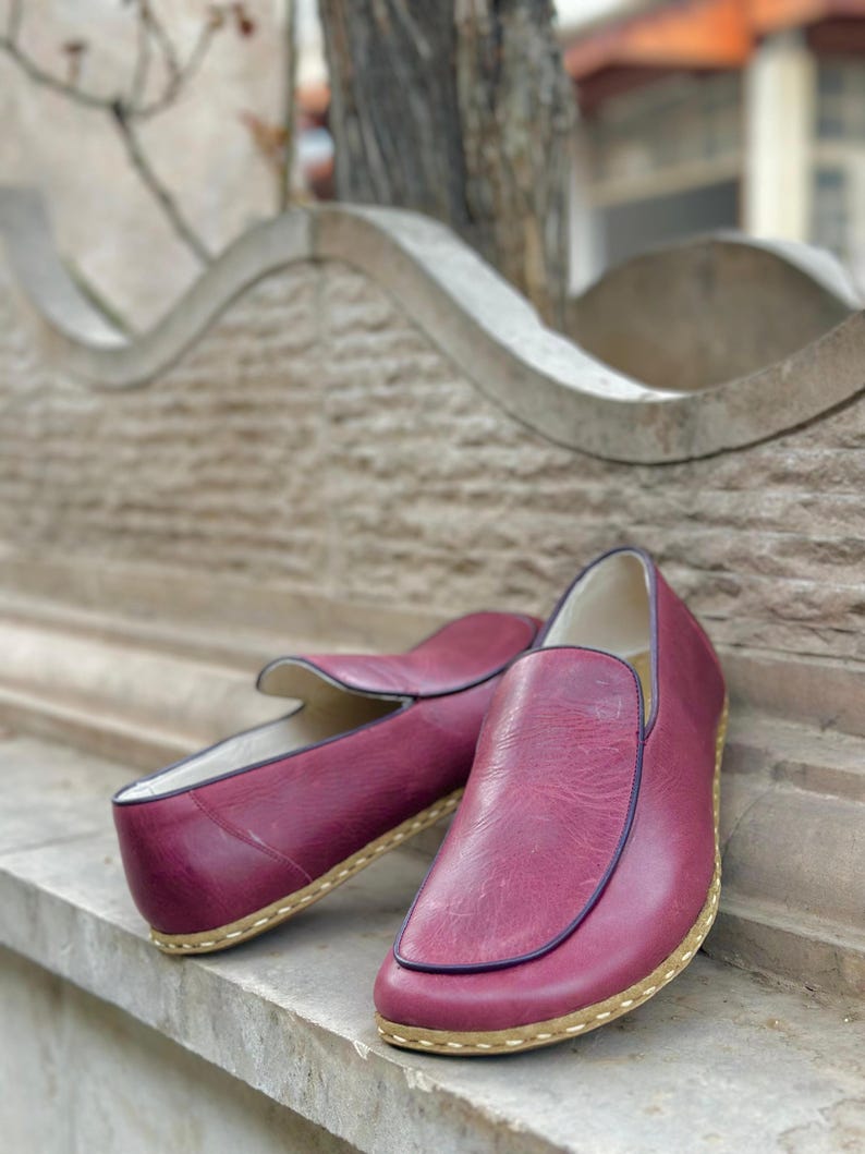 Puede incluir: Un par de zapatos de cuero burdeos con suela marr&oacute;n claro. Los zapatos est&aacute;n sobre una superficie de piedra.