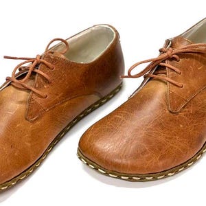 May include: A pair of brown leather lace-up shoes with a stitched sole.